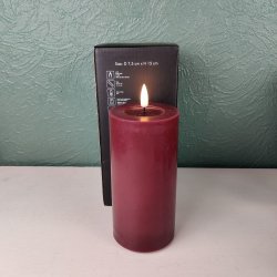 Milj�billede af det t�ndte bordeauxfarvede LED-bloklys p� D 7,5 cm x H 15 cm st�ende foran den tilh�rende sorte produkt�ske.