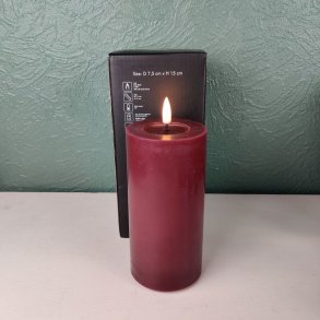 Milj�billede af det t�ndte bordeauxfarvede LED-bloklys p� D 7,5 cm x H 15 cm st�ende foran den tilh�rende sorte produkt�ske.
