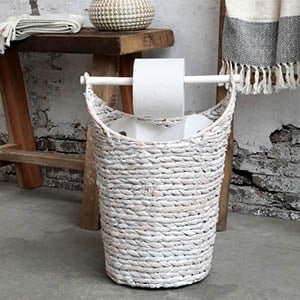 hvid flettet kurv som toiletrulleholder st�r p� badev�relset ved siden af en grov b�nk i tr� hvor der ligger et h�ndkl�de 