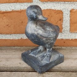 M�rkegr� �lling-figur med rustik overflade, opstillet p� en gammel tr�b�nk i haven.