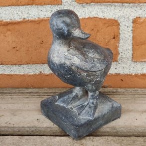 M�rkegr� �lling-figur med rustik overflade, opstillet p� en gammel tr�b�nk i haven.