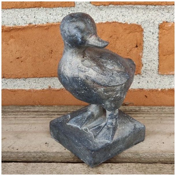 M�rkegr� �lling-figur med rustik overflade, opstillet p� en gammel tr�b�nk i haven.