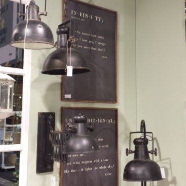 factory-lamper-chic-antique-industriel-charme.jpg: En samling af sorte, patinerede Factory metallamper fra Chic Antique, herunder en sakse-v�glampe og en loftslampe, udstillet foran vintage tavleskilte med fransk tekst i et milj�, der kombinerer industrie