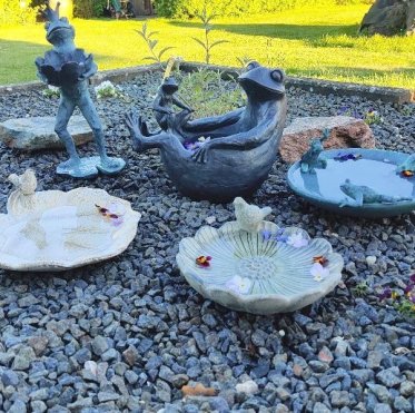 fuglebad-keramik-fuglefigurer-fr�figurer-granitskaerver-haveinterioer.jpg: En samling af forskellige fuglebade i glaseret keramik og metal med dekorative fugle- og fr�figurer, placeret i et havemilj� p� granitsk�rver.