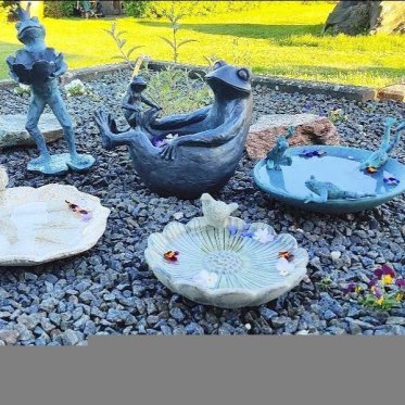 fuglebade-stoebejern-polyresin-havefigurer-fugle-froeer.jpg: Stemningsbillede med forskellige fuglebade placeret p� gr� granitsk�rver; forrest ses to blomsterformede fade med fuglefigurer, til h�jre et bl�t fad med fr�er, og i baggrunden ses en st�ende fr