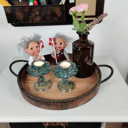 To gr�nne blomsterformede fyrfadsstager i glas p� stilk med t�ndte lys placeret p� en rund tr�bakke sammen med to nisse- og troldefigurer med dannebrogsflag.