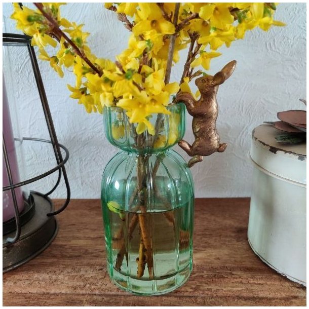 Gr�n rillet glasvase med en gul forsythiagren og en lille bronzefarvet p�skehare i kanten.