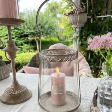 Fransk-inspireret hurricane lysestage med h�j hank og metalfod, dekoreret med et lyser�dt LED bloklys p� et d�kket havebord.