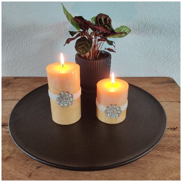 N�rbillede af to t�ndte gule bloklys med en lysere bund og m�rkere gul top, dekoreret med hvide b�nd og store rhinsten-blomster.