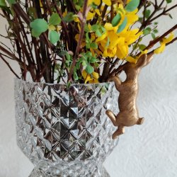 Lille guld p�skehare dekoration opstillet p� kanten af en krystalvase med for�rsgren og gule blomster.