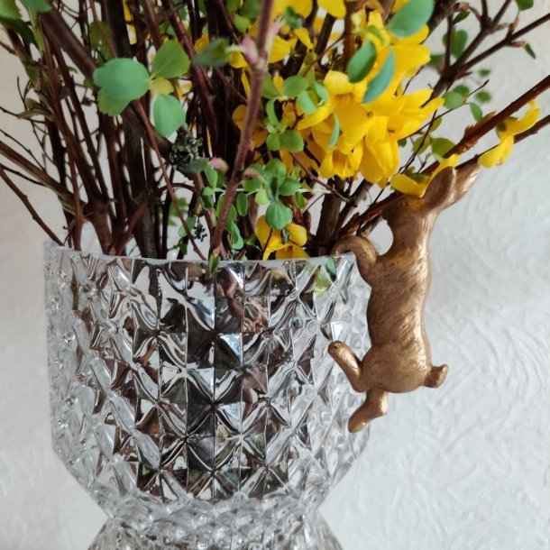 Lille guld p�skehare dekoration opstillet p� kanten af en krystalvase med for�rsgren og gule blomster.