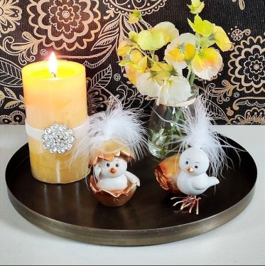 p�skepynt p� rund dekobakke med p�skekyllinger med guld�g gul bloklys og gule blomster i vase som kaetoribillede for p�skepynt