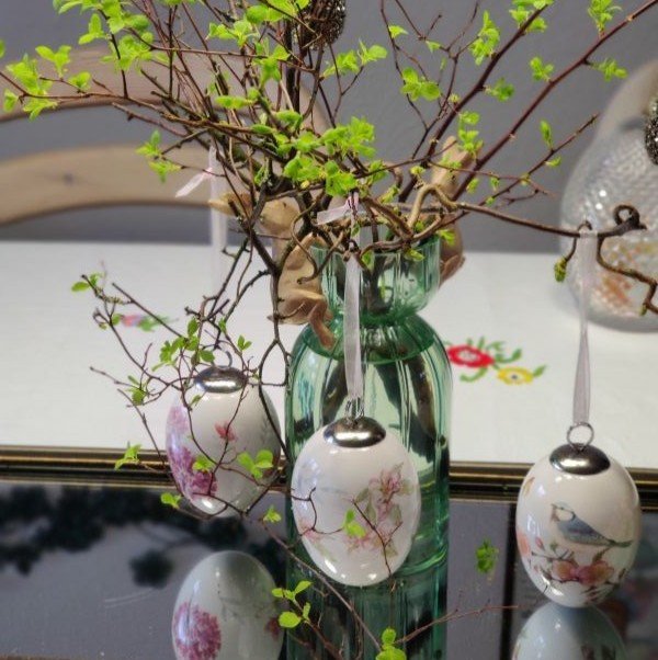 Elegant for�rsdekoration med friske grene i en gr�n glasvase, pyntet med tre smukke p�ske�g med blomster- og fuglemotiver fra Norgaard Bolignyt.