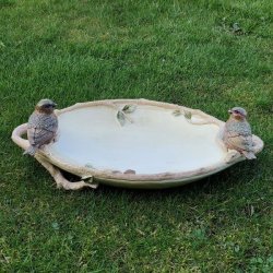 Dekorativt sandfarvet fuglebad med to fuglefigurer placeret p� en gr�n gr�spl�ne.