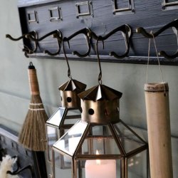 N�rbillede af to dobbelte metal-knager og to tilh�rende metal-m�rkerammer p� den m�rke kul-farvede knager�kke, med en t�ndt messing-lanterne h�ngende.