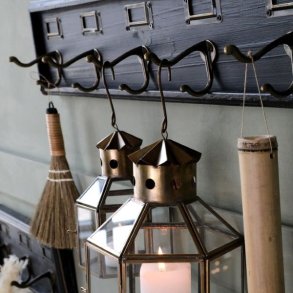 N�rbillede af to dobbelte metal-knager og to tilh�rende metal-m�rkerammer p� den m�rke kul-farvede knager�kke, med en t�ndt messing-lanterne h�ngende.