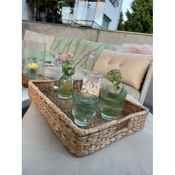 Udend�rs stemningsbillede med gr�nne rillede glasfyrfadsstager og sm� vaser placeret i en flettet bakke p� en terrasse.