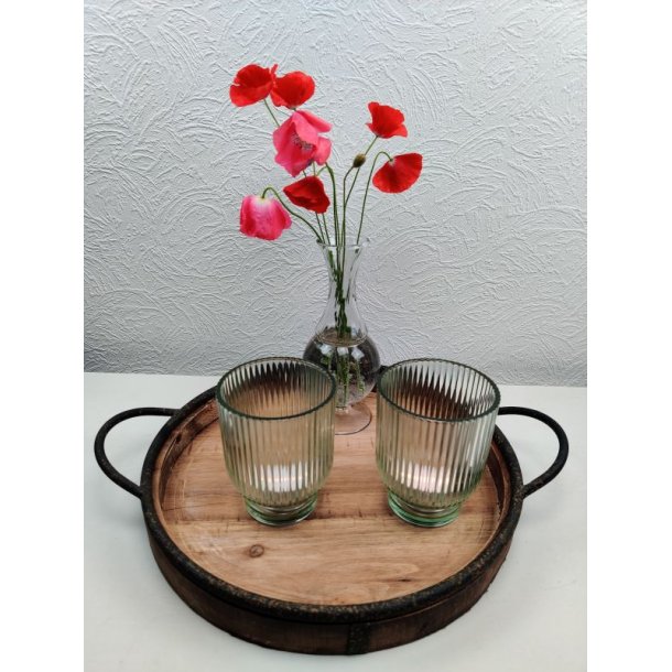 To gr�nne rillede fyrfadsstager i glas p� en rund tr�bakke med jernh�ndtag ved siden af en lille vase med r�de valmuer.