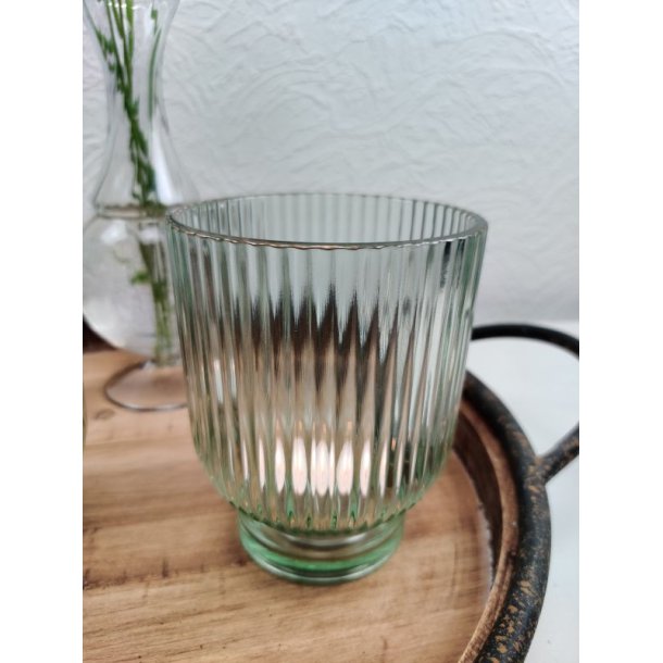 N�rbillede af en gr�n fyrfadstage i rillet glas placeret p� en rustik tr�bakke med t�ndt lys indeni.