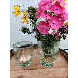 Gr�n rillet glasfyrfadstage med t�ndt lys ved siden af matchende glasvase med en buket farverige sommerblomster p� et tr�fad.