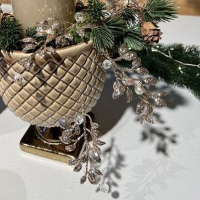 Kunstig-Bladranke-Guld-Perler-Miljoe-Vase Dekorativ guldbladranke med perler slynget omkring en harlekinm�nstret keramikvase med granris, kogler og et stort t�ndt bloklys.