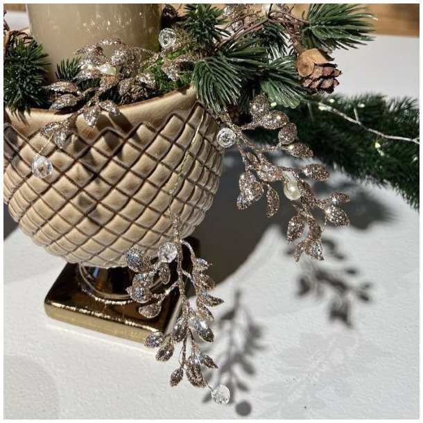 Kunstig-Bladranke-Guld-Perler-Miljoe-Vase Dekorativ guldbladranke med perler slynget omkring en harlekinm�nstret keramikvase med granris, kogler og et stort t�ndt bloklys.