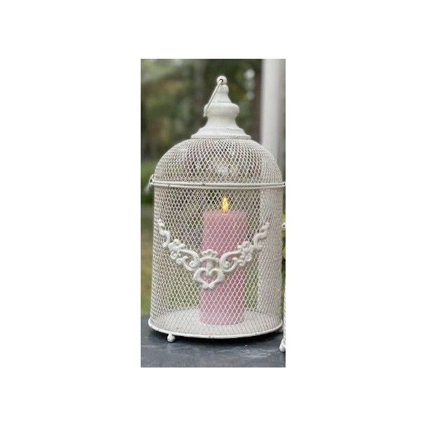 Milj�billede af det antik hvide lanternebur med et t�ndt rosa bloklys indeni. Lyset skinner hyggeligt gennem metalnettet i en udend�rs opstilling.