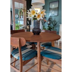 Stemningsbillede af m�rk rillet retro glasvase med liljer midt p� et rundt retro tr�spisebord i en stilfuld stue.