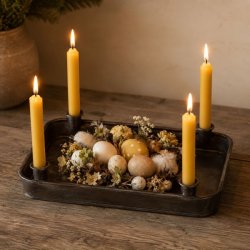 Jernfad med fire lysholdere pyntet til p�ske med gule stagelys, mos, p�ske�g og sm� blomster p� et tr�bord.