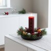 Stemningsfuldt firkantet milj�billede af det t�ndte bordeauxr�de adventslys i en juledekoration med grangrene p� en hvid sk�nk
