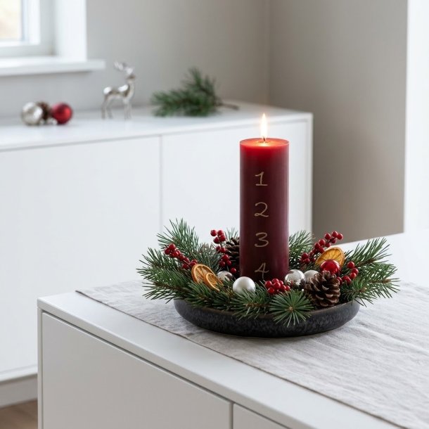 Stemningsfuldt firkantet milj�billede af det t�ndte bordeauxr�de adventslys i en juledekoration med grangrene p� en hvid sk�nk