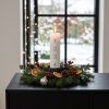 Stemningsfuldt firkantet milj�billede af det t�ndte hvide adventslys i en juledekoration med grangrene p� en sort sk�nk.