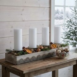 Rustik juledekoration i en tr�kasse med fire hvide bloklys, gran, kogler, valn�dder og t�rrede appelsinskiver, placeret p� et tr�bord. I baggrunden ses en hvid tr�v�g og et vindue med udsigt til et sned�kket landskab og et juletr�.