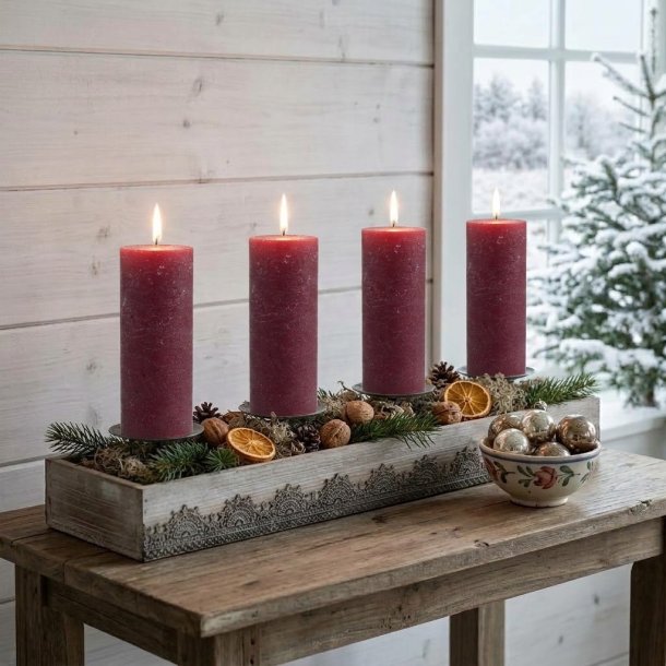 Stemningsfuldt firkantet milj�billede af adventsstagen i tr� pyntet med mose, kogler og t�rrede appelsinskiver samt fire t�ndte bordeauxr�de bloklys p� et tr�bord.