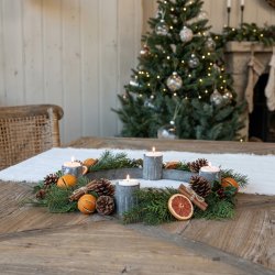 Stemningsfuldt firkantet milj�billede af den runde adventsstage i antik zink med t�ndte fyrfadslys, pyntet med grangrene, kogler og t�rrede appelsinskiver p� et tr�bord.