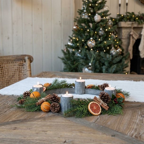 Stemningsfuldt firkantet milj�billede af den runde adventsstage i antik zink med t�ndte fyrfadslys, pyntet med grangrene, kogler og t�rrede appelsinskiver p� et tr�bord.