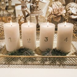 Stemningsfuldt firkantet milj�billede af adventstal 1 til 4 fastgjort p� fire hvide bloklys, opstillet i en gylden tr�dbakke med grangrene og julepynt i baggrunden.