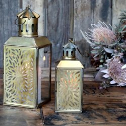 De to st�rrelser lanterner st�r t�ndte ved siden af hinanden p� et rustikt tr�bord indend�rs og skaber en varm atmosf�re.