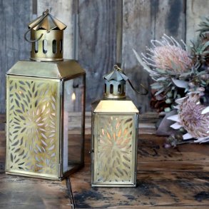 De to st�rrelser lanterner st�r t�ndte ved siden af hinanden p� et rustikt tr�bord indend�rs og skaber en varm atmosf�re.