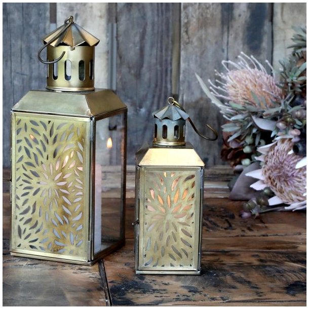 De to st�rrelser lanterner st�r t�ndte ved siden af hinanden p� et rustikt tr�bord indend�rs og skaber en varm atmosf�re.