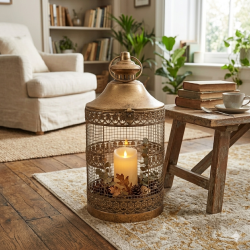 Stemningsbillede fra en hyggelig stue, hvor et rustikt, rundt lanternebur i antique guld med t�ndt LED-bloklys og efter�rspynt st�r p� et m�nstret gulvt�ppe ved siden af et rustikt tr�bord.