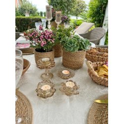 Fire beige farvede fyrfadsstager i glas formet som blomster med t�ndte lys p� et veld�kket bord p� terrassen.