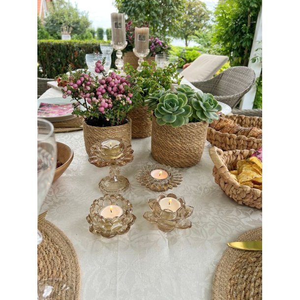 Fire beige farvede fyrfadsstager i glas formet som blomster med t�ndte lys p� et veld�kket bord p� terrassen.