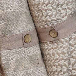 N�rbillede af det praktiske beige lukkeb�nd med en fin tr�knap, der holder den sammenrullede bomuldsplaid p�nt p� plads.