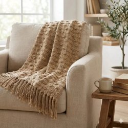 Et n�rbillede af den beige m�nstrede plaid med frynser, draperet over en stilfuld stol i et hyggeligt indend�rs milj�.