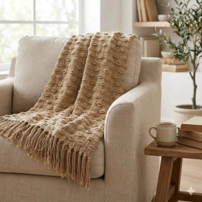 Et n�rbillede af den beige m�nstrede plaid med frynser, draperet over en stilfuld stol i et hyggeligt indend�rs milj�.