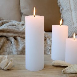 Stemningsfuldt milj�billede af t�ndte hvide bloklys placeret p� et tr�bord med bl�de tekstiler og naturlige elementer i baggrunden.