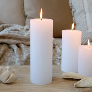 Stemningsfuldt milj�billede af t�ndte hvide bloklys placeret p� et tr�bord med bl�de tekstiler og naturlige elementer i baggrunden.
