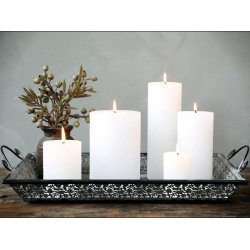 Dekorativt milj�billede af flere hvide bloklys i forskellige h�jder arrangeret p� en m�nstret metalkuffert eller bakke sammen med en vase med kviste.