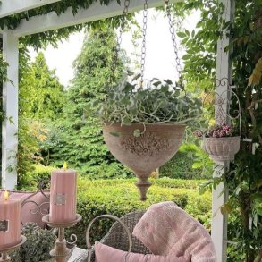 En rustik blomsterpotte i antik sandfarvet jern h�nger dekorativt i en gr�n have. Potten er monteret med en metalk�de og indeholder en lille gr�n plante.